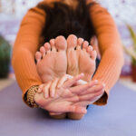 Frau sitzt auf Yogamatte und umklammert ihre Füße